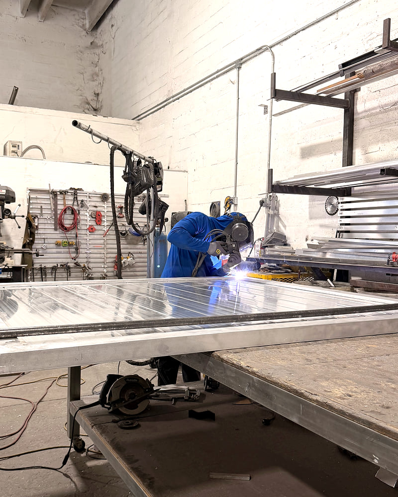 Soldador de Milos Pro trabajando en el taller sobre un portón de aluminio, con el arco encendido